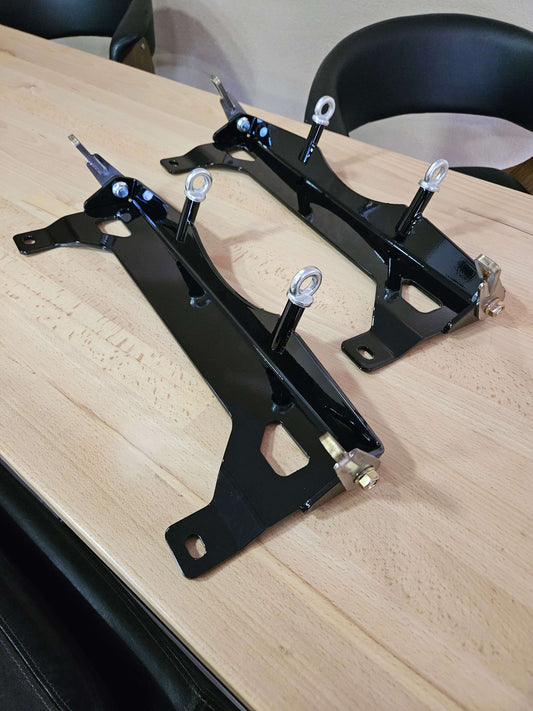 AMG GT Lower Harness Bracket pair with steel construction and adapters for racing harnesses on a wooden table.
