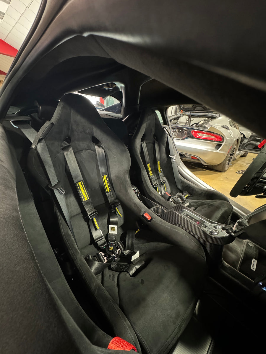 Interior view of McLaren sports car showing racing seats with 6-point harnesses installed.